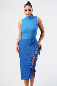 vibrant blue sleeveless midi dress with a high neckline, featuring a textured top and a skirt with a unique wave pattern. The dress includes an eye-catching side slit adorned with a lace-up detail and tassel ties, set against a simple backdrop to highlight its striking design.