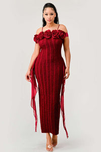 off-shoulder red midi dress with an intricate lace pattern and a decorative row of roses along the neckline. Ethereal tulle streamers flow from the waist, and the look is completed with transparent high-heeled sandals.