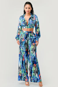 The ensemble features a bold and vibrant print that captures the essence of tropical flora and the free-spiritedness of island life. The top, with its flared sleeves and tie-front detail, pairs beautifully with the flowing palazzo pants